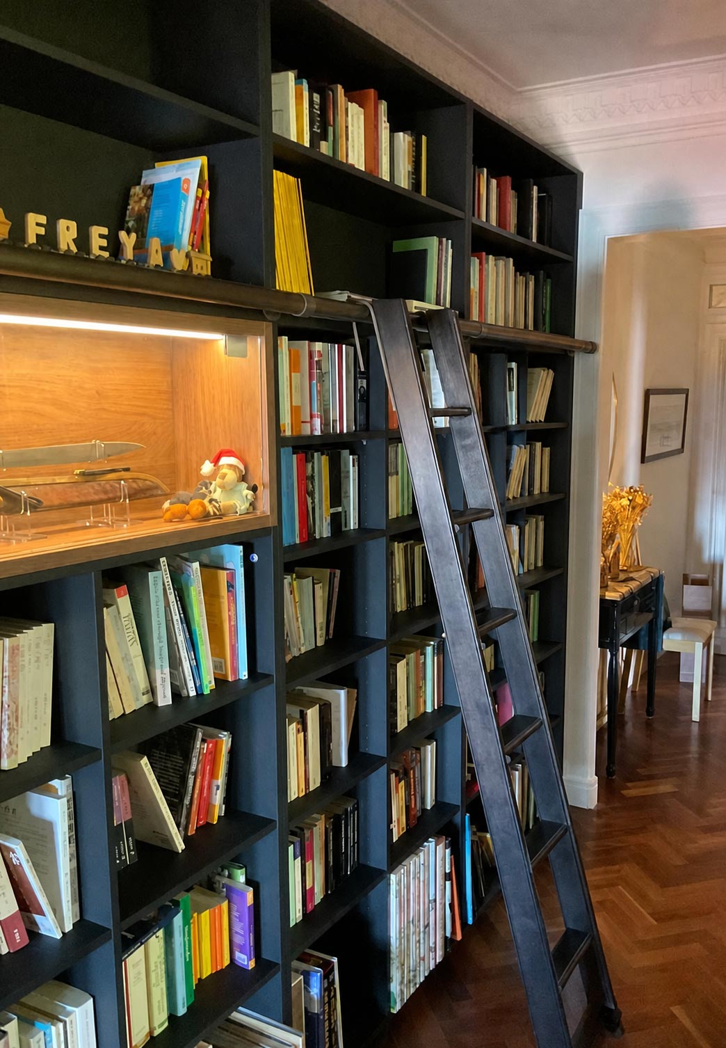 A woman on a ladder reaching for a book on a high shelf in a well-organized library setting